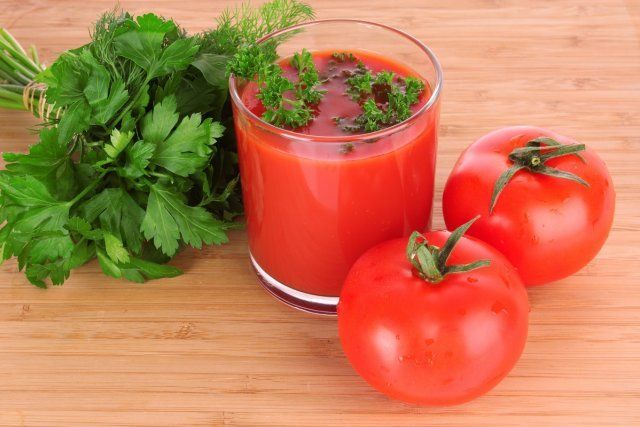 Vaso de jugo de tomate fresco y tomates alrededor del vaso sobre la mesa.