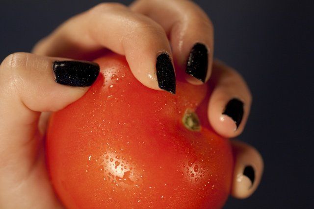 Vista de unas manos de mujer sosteniendo un tomate rojo.