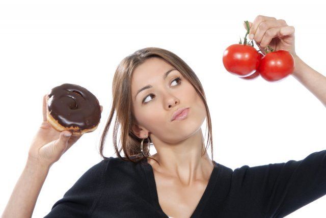 Concepto de alimentación saludable. Mujer comparando una dona poco saludable con tomates rojos orgánicos, pensando que está aislada sobre un fondo blanco